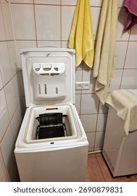 A top-loading washing machine with the open lid stands in the bathroom
