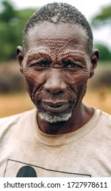 TOPOSA TRIBE, SOUTH SUDAN - MARCH 12, 2020: Elderly male in dirty t shirt and with traditional scars on face looking at camera while living in Toposa Tribe village in South Sudan, Africa