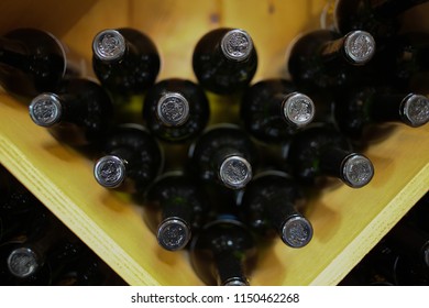 Tops of Black Glass Wine Bottles Stacked in a Wooden Shelf - Top View of Bottled Wine Stored on Rack for Aging