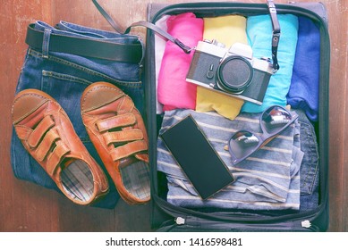 Topview open travel bag which have clothes and accessories on wood background