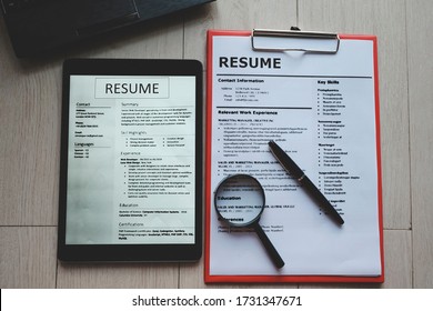 Top-view of resume with tablet computer, magnifying glass,  computer laptop and pen on wooden background - Powered by Shutterstock