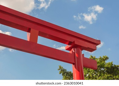 Torii or 鳥居 in Japanese. Liberdade neighborhood, São Paulo, Brazil. Gate for entry to a sacred space. In the background the blue sky with white clouds and tree foliage.