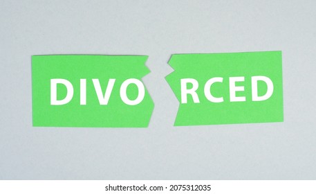 Torn apart green paper with the word divorced on a grey background, end of marriage, separation