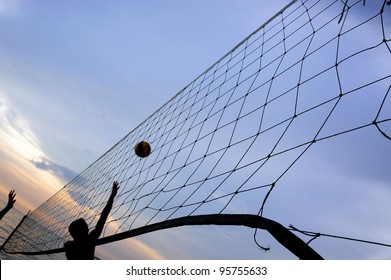 Torn beach volleyball net at tropical beach during sunset.