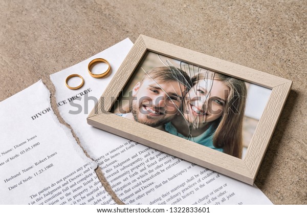Torn divorce decree, rings and broken frame with\
photo on table