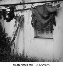 Torn garden tent and window shutter. Abandoned house exterior black and white.