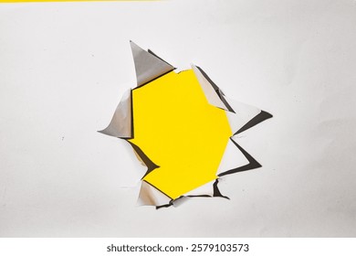 A torn hole in a white paper with a bright yellow background. Perfect for product presentations, branding, and advertising.