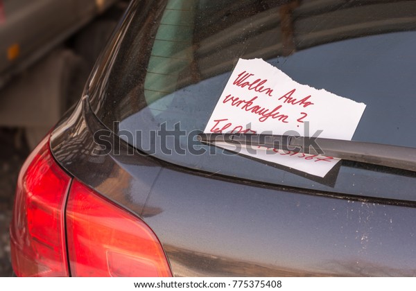 Torn note on the rear window wiper of a car with\
the German inscription - Do you want to sell your car - and a\
hidden phone number