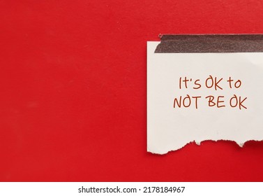 Torn note paper stick on red copy space background with text written IT'S OK TO NOT BE OK, means feelings and emotions expressing are valid no matter what they are, its normal to say you are not okay