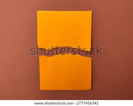 Torn orange sticky note halves on brown surface.