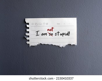 Torn paper on gray wall with handwrtten text I AM NOT STUPID, changed to I AM NOT STUPID, to overcome negative self talk and raise self esteem