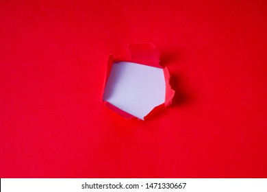 Torn red colored paper on white background with closeup hole in the sheet of paper. Background concept with copy space.