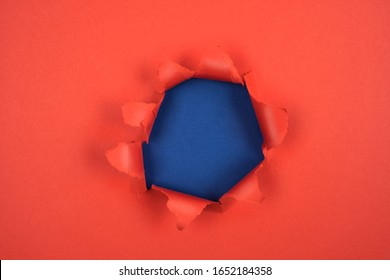 Torn round hole in red paper with torn edges and a blue background. Space for message, paper texture.