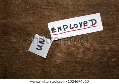 Torn, white paper sheet with inscription unemployed on the brown wooden office desk. Unemployment status is over. Found new job. Hiring concept.