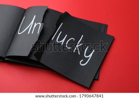 Torn word UNLUCKY written in notebook on red background