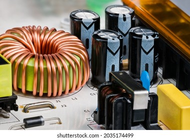 Toroidal core inductor, transformer or electrolytic capacitors on PCB detail. Close-up of coil wrapped by copper wire. Electrical components on white printed circuit board of switch-mode power supply.