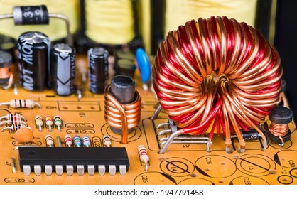Toroidal or cylindric inductors on printed circuit board with electronic components. Closeup of magnetic core coils, microchip and resistors or capacitors on orange PCB detail. Electrical engineering.