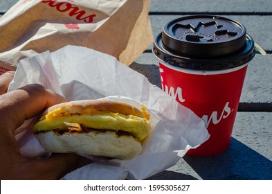 Toronto, Canada - 12/22/2019: Person Holding Bacon English Muffin From Tim Horton's Breakfast Menu With A Cup.