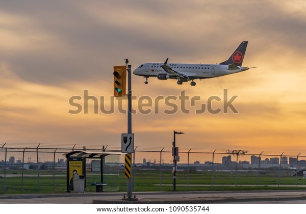 TORONTO, CANADA - Air Canada Boeing 737\
is landing over a bust stop and a street stop light on Avenue Road\
at Toronto Lester B. Pearson Airport at\
sunset