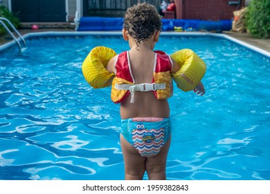Toronto, Canada, August 2020 - Toddler boy in water wings stands at edge of swimming pool ready to jump into water