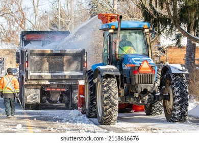 Toronto, Canada, February 5, 2022; Street Snow Removal Snow Blower And Dump Truck Clearing Snow From The Roadway After A Large Snowfall Including A Flag Man Or Woman Guiding The Work