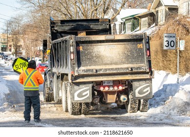 Toronto, Canada, February 5, 2022; Street Snow Removal Sdump Truck Ready For Snow Blower Clearing Snow From The Roadway After A Large Snowfall Including A Flag Man Or Woman Guiding The Work