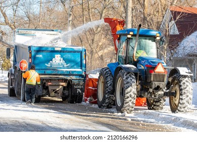 Toronto, Canada, February 5, 2022; A City Street Snow Removal Snow Blower And A Farm Dump Truck Clearing Snow From The Roadway After A Blizzard Including A Flag Man With Stop Sign Guiding The Work