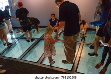 TORONTO, CANADA - JUNE, 2016: Man Walking On The Glass Floor Of The CN Tower, 350 Meters Above Ground Level. Visitors Are Allowed To Walk Or Crawl Across The Glass Floor Or Sit Or Even Jump On It.