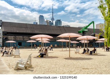 Toronto, Canada - June 6, 2018: People Sitting In The Adirondack Chairs On Toronto Beach With CN Tower In The Distance