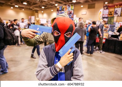 TORONTO, CANADA - MARCH 17, 2017: Kid in DEADPOOL mask holding toy gun with toy gun pointed at his head by friend at 2017 TORONTO COMIC CON. 