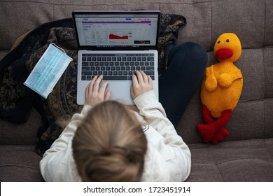 Toronto, Canada - May, 2,2020: Top View Of Woman Sitting On Sofa Using Laptop, With Facial Mask And Stuffed Toy. Work From Home On The Coronavirus Quarantine Concept