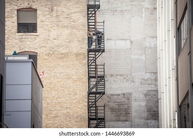 TORONTO, CANADA - NOVEMBER 14, 2018: Construction workers fixing Fire escape rusty stairs and ladders, in metal, on a typical North American old brick building. These stairs are made for emergency