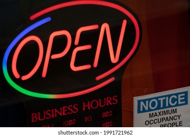 Toronto, ON Canada - June 13 2021: Open Business Hours And Maximum Capacity Neon Storefront Sign In Toronto, Ontario Canada. Patio Season Opening Sign Posted During Phase One Of The Three Stage Plan.