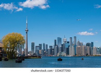 Toronto, ON, Canada, June 8,2019 - View Of The Toronto Skyline From Toronto Island With A Plane Taking Off Overhead.