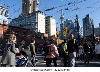 Toronto, ON, Canada - October 5, 2022: People Walk Across Queen St. At Spadina Ave. In The Afternoon Rush Hour, The CN Tower Can Be Seen In The Far Background.