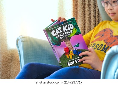 Toronto, Ontario, Canada - April 17, 2022:  Boy student reading latest graphic novel comics book Cat Kid on sofa. Child education and reading club activities background.