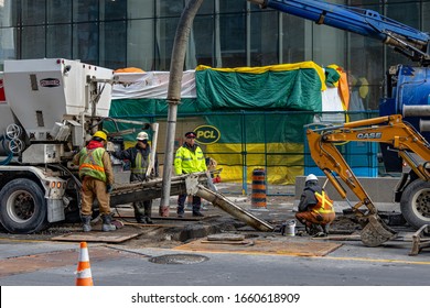 Toronto, Ontario, Canada - Feb 25, 2020 : Road Work Crew Surrounded By Heavy Machinery With A Traffic Cop Standing Guard On A Downtown Toronto Street On A Winter Day. 