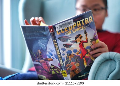 Toronto, Ontario, Canada - January 22, 2022 : Student boy reading graphic novel book Cleopatra in space borrowed from public library at home. 