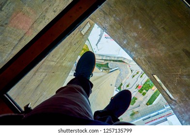 Toronto, Ontario, Canada - June 2016:  Man's Feet On The Glass Floor Of The CN Tower, 350 Meters Above Ground Level. Visitors Are Allowed To Walk Or Crawl Across The Glass Floor Or Sit On It.