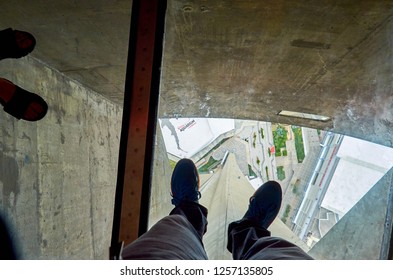 Toronto, Ontario, Canada - June 2016:  Man's Feet On The Glass Floor Of The CN Tower, 350 Meters Above Ground Level. Visitors Are Allowed To Walk Or Crawl Across The Glass Floor Or Sit On It.