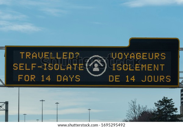 Toronto, Ontario, Canada - Mar 4, 2020: Sign\
Travelled? Self isolate for 14 days on a scoreboard over highway\
during corona virus covid 19 pandemic outbreak quarantine lockdown.\
Selective focus.