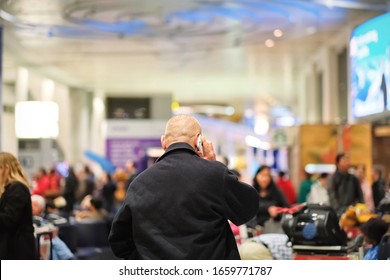 Toronto, Ontario, Canada- March 25,2019: Back view of man make phone from smart phone on a blurred Pearson international airport background. Selective focus.