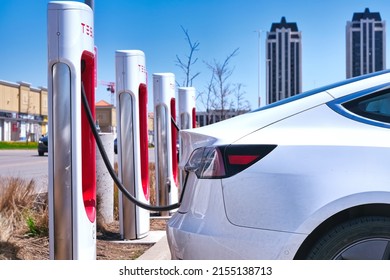 Toronto, Ontario, Canada - May 08, 2022: Tesla electric car charging at supercharger station on city street. EV green energy and environmental background. 
