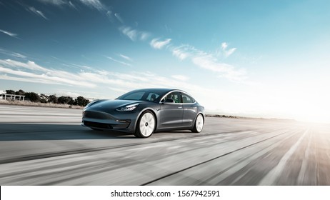 Toronto, Ontario / Canada - November 22nd 2019 : Photograph of a grey Tesla model 3 driving on the road with the sun setting in the background.
