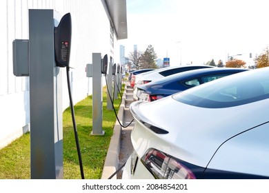 Toronto, Ontario, Canada - November 6, 2021 : Selective focus of Tesla electric cars in a row and recharging at supercharger charging stations in parking lot. EV green energy transportation background