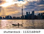 TORONTO SKYLINE - Canoe being paddled past Toronto buildings and skyscrapers at sunset. Silhouetted canoer exploring outdoors in urban city setting. Sunlight shining on waves of Lake Ontario. Canada