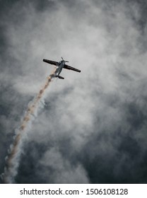 Toronto/Canada - August 30, 2019: Famous pilot flying a YAK-50 at the Air Show while executing great technical maneuvers and leaving white smoke on the dark sky.