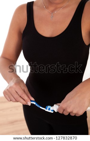 Torso of an athletic woman applying toothpaste from a tube to a plastic domestic toothbrush