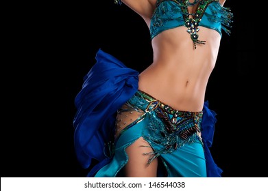 Torso of a female belly dancer wearing a teal blue costume and shaking her hips. Isolated on a black background. 