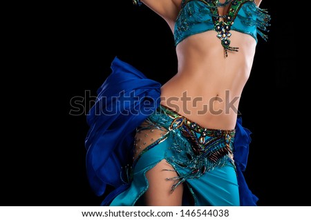 Torso of a female belly dancer wearing a teal blue costume and shaking her hips. Isolated on a black background. 